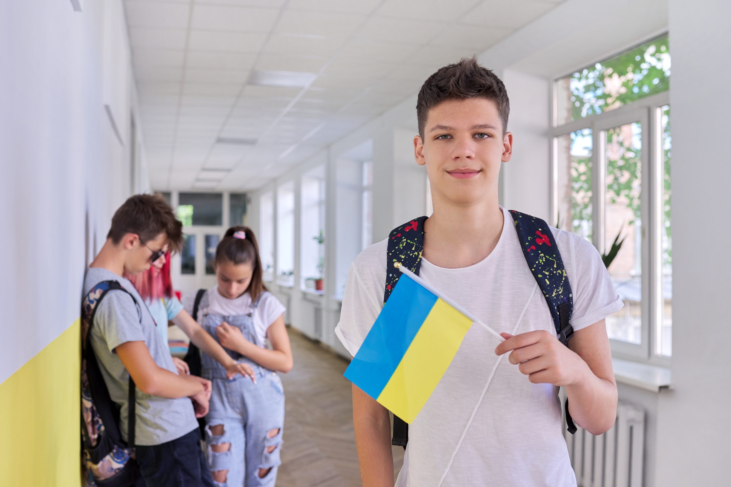Teenager student with Ukraine flag, school corridor group of students background. Ukraine school education youth people concept